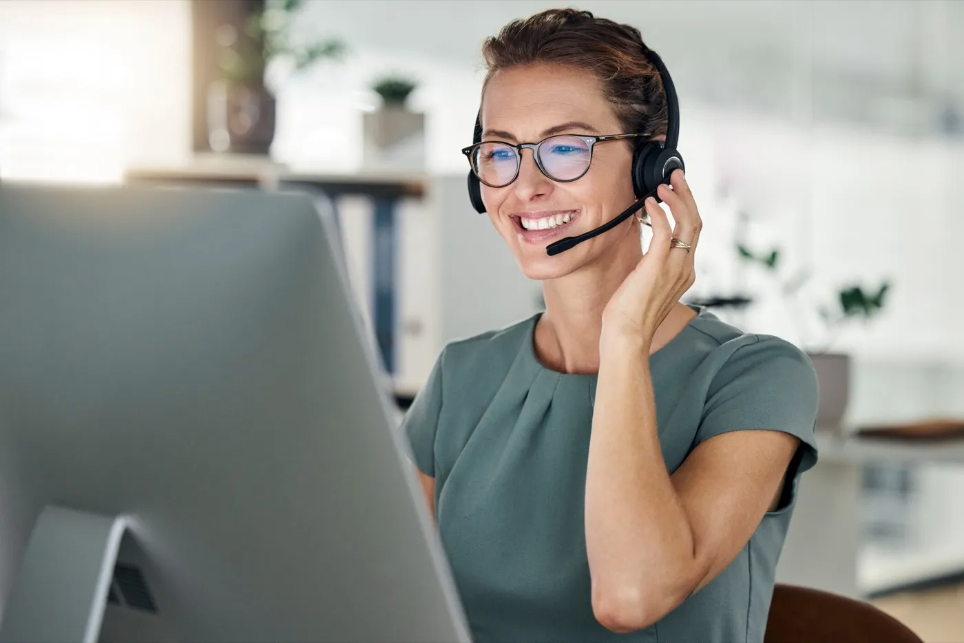 A front desk coordinator on a headset call, smiling at her screen